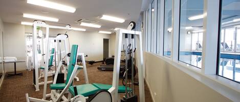 A gym with various exercise machines, large windows, and a carpeted floor.