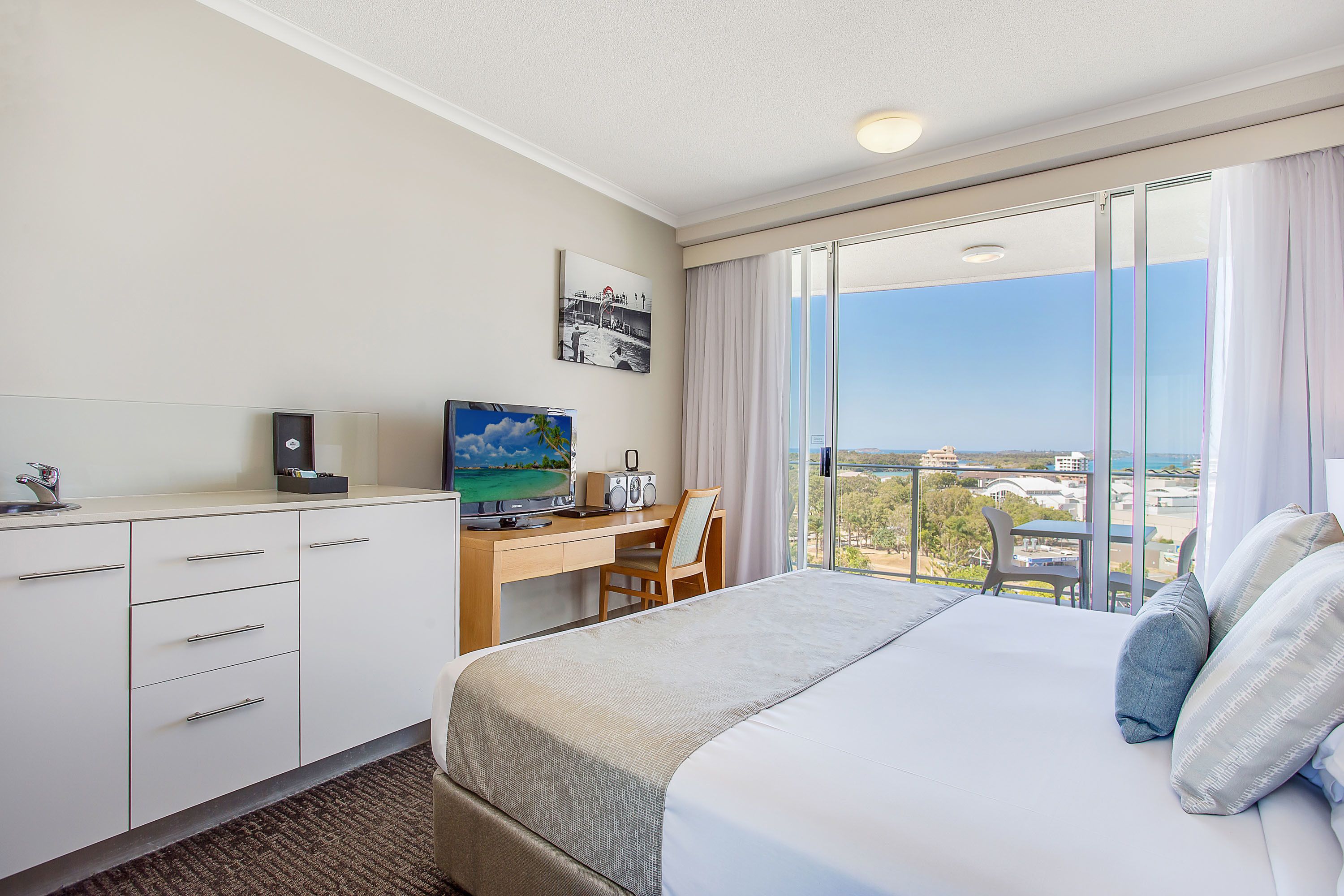 Habitación de hotel con cama, escritorio, silla, televisor y vista a la ciudad.