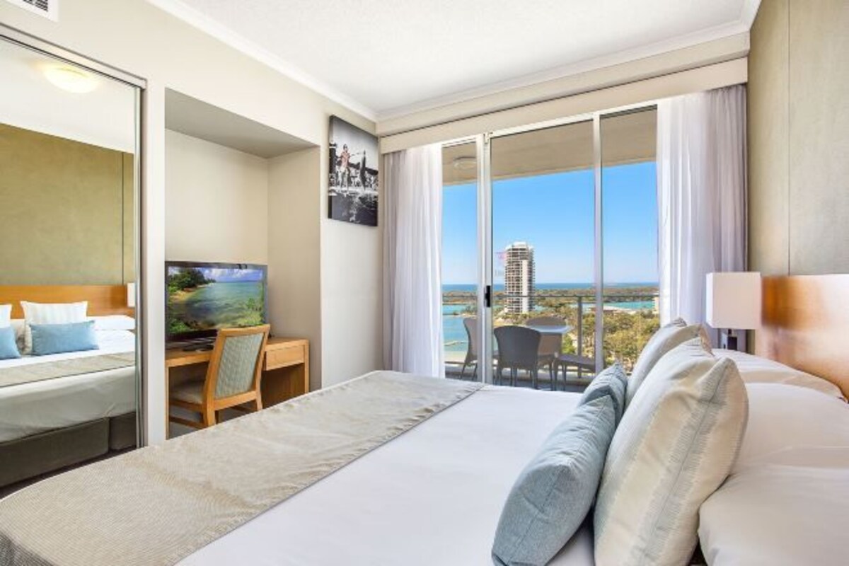 A hotel room with a bed, a desk with a TV, a balcony with a view of the city.