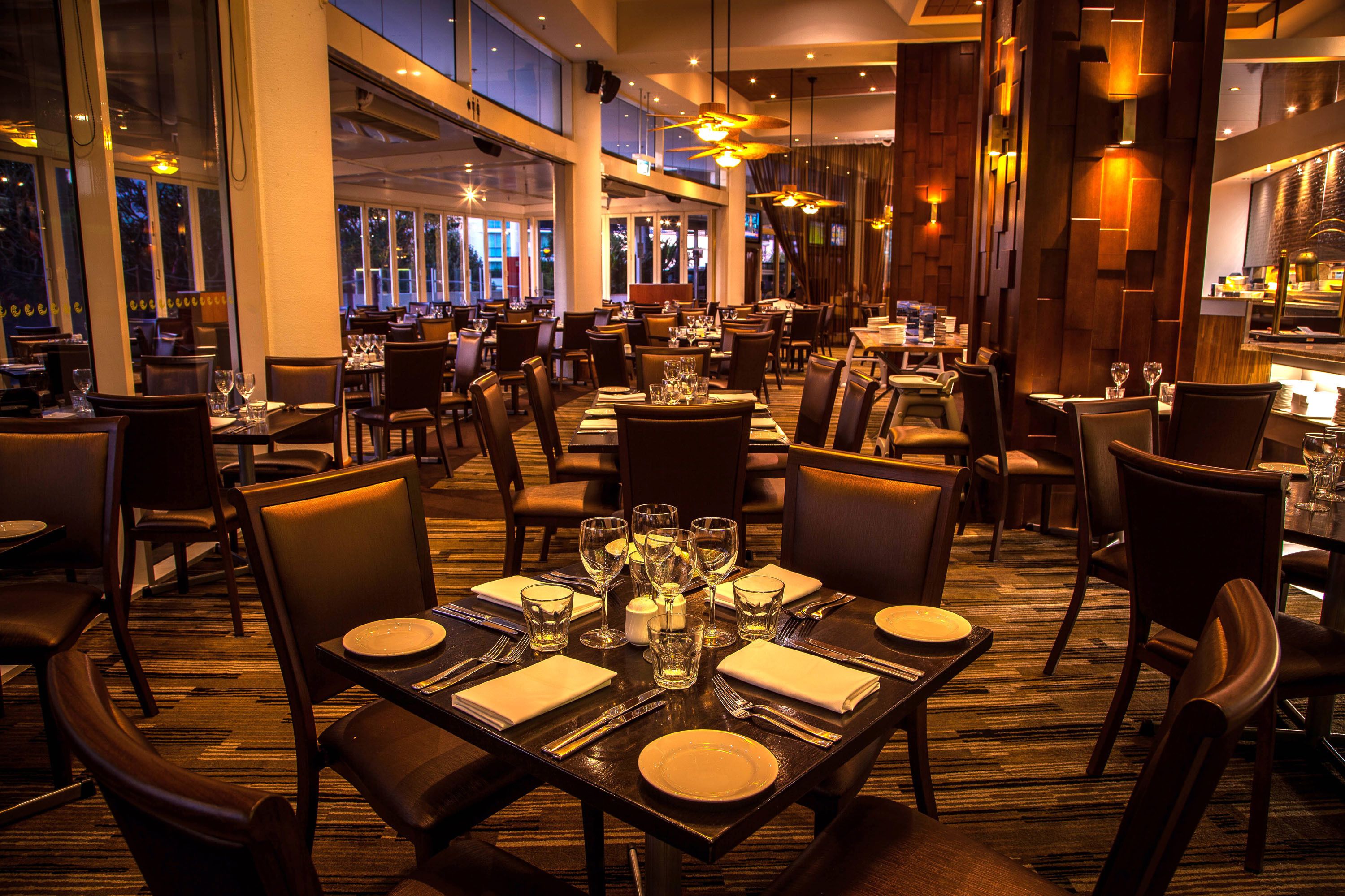 A restaurant with multiple tables set for dining, large windows, and a warm interior lighting.