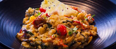 A plate of risotto with cherry tomatoes, herbs, and a piece of bread on a dark plate.