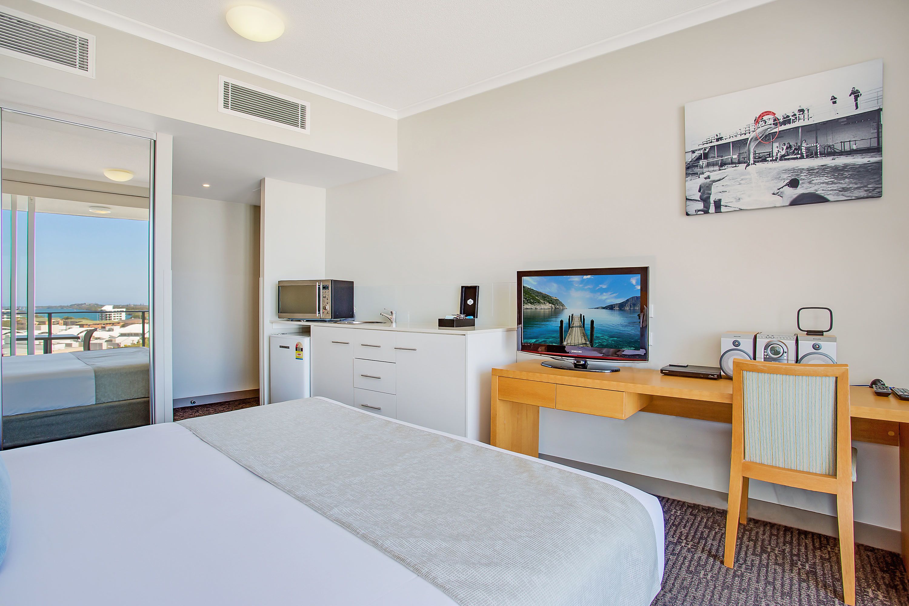 A hotel room with a bed, a desk with a computer, a TV, and a view of the city.