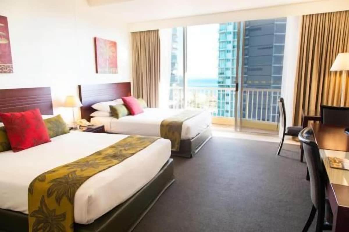 A hotel room with two beds, a desk, and a view of a cityscape.