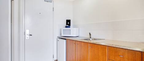 A compact kitchen with white cabinets, a microwave, and a small refrigerator.