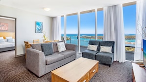 A modern hotel room with a large balcony, grey sofas, a wooden coffee table, and a dining area with a view of the sea. - Mantra Twin Towns (Tweed Heads)