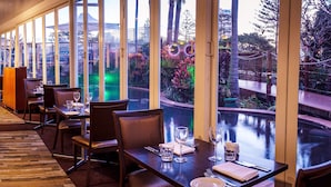 A restaurant with a view of a water feature and greenery. Tables are set with glasses and cutlery. - Mantra Twin Towns (Tweed Heads)