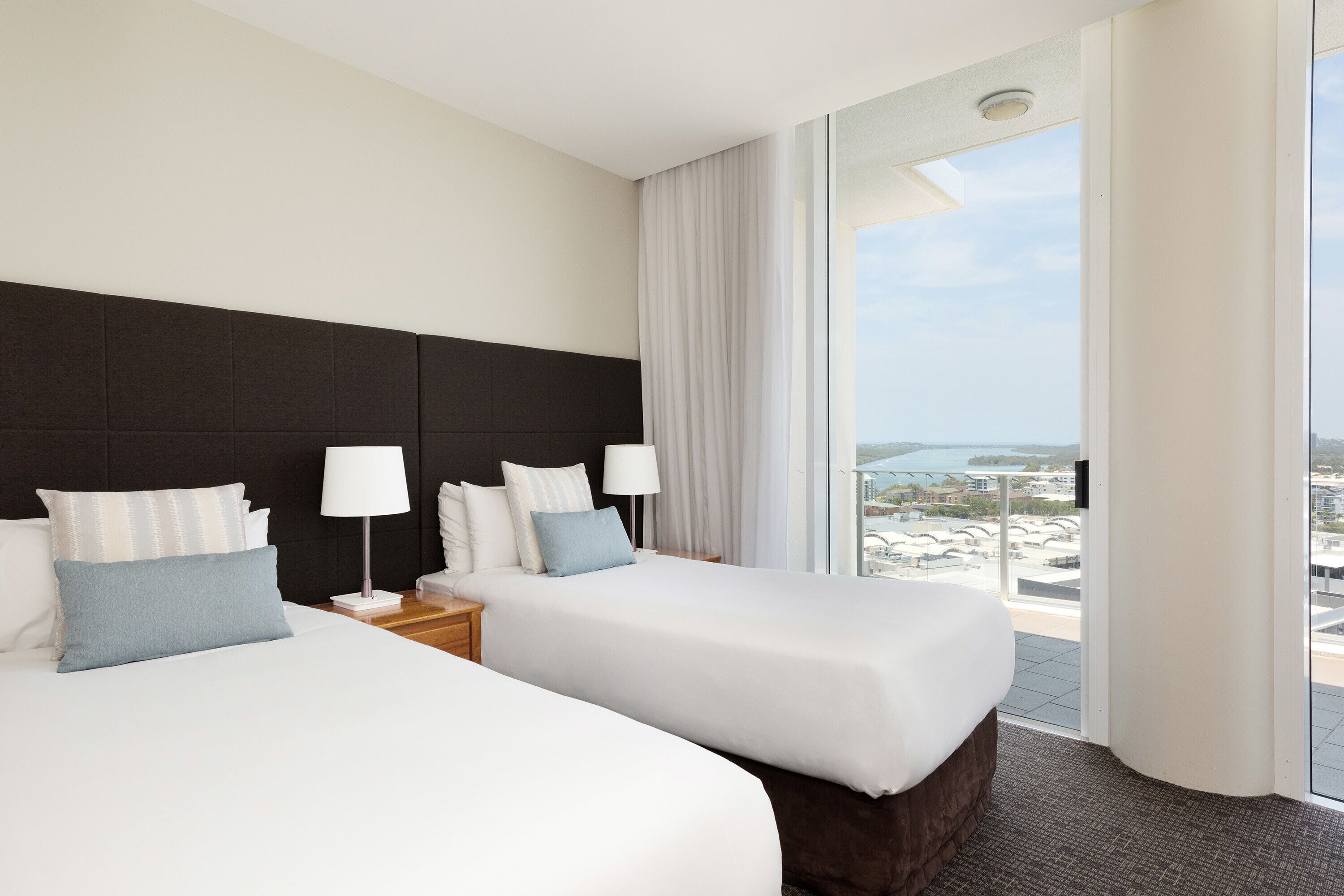 Une chambre d’hôtel avec deux lits, une grande fenêtre offrant une belle vue et un design moderne.