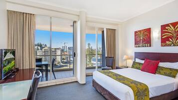 A hotel room with a bed, a desk, a TV, and a balcony with a city view.