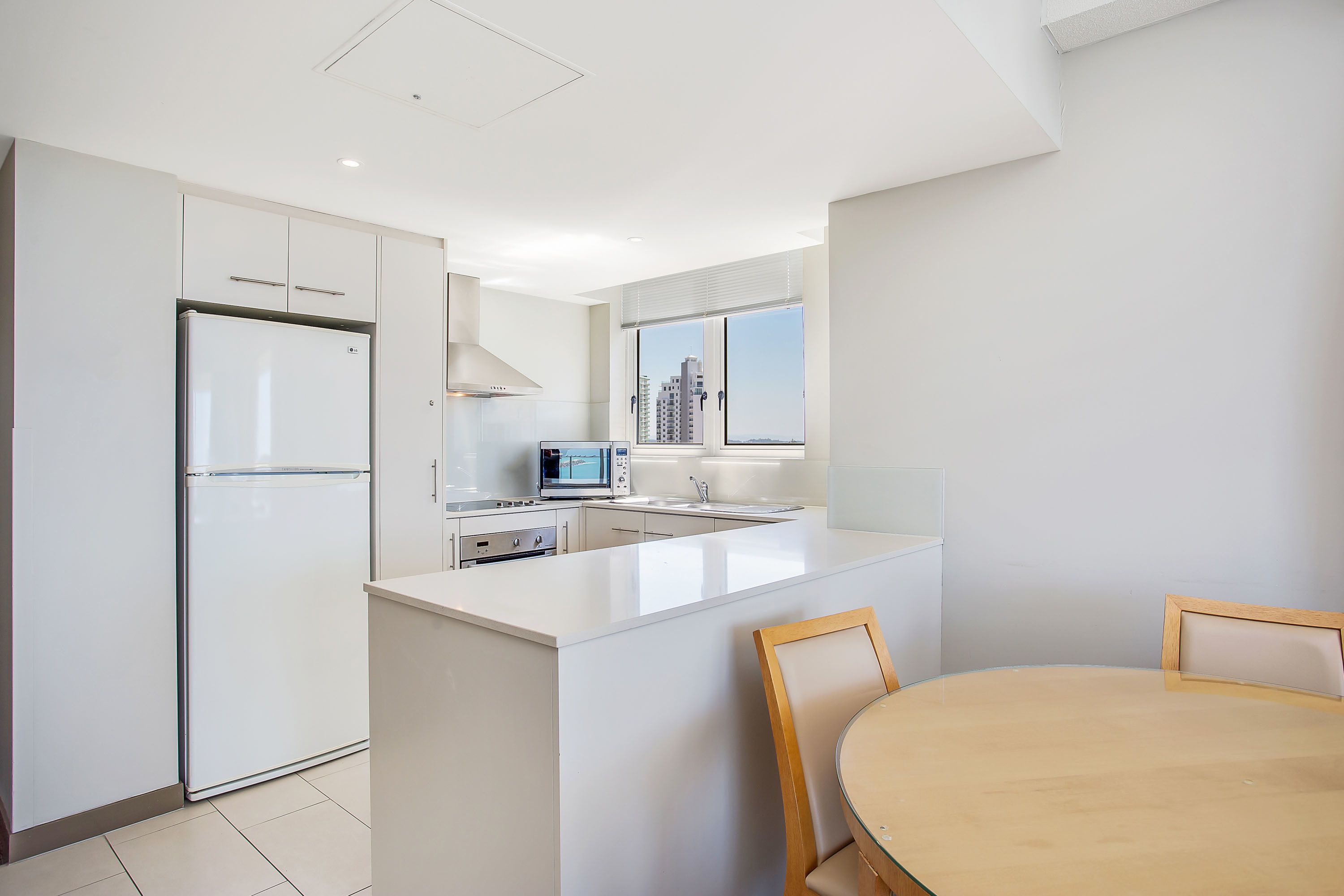 A modern kitchen with white cabinetry, a built-in microwave, and a large island with a round table.