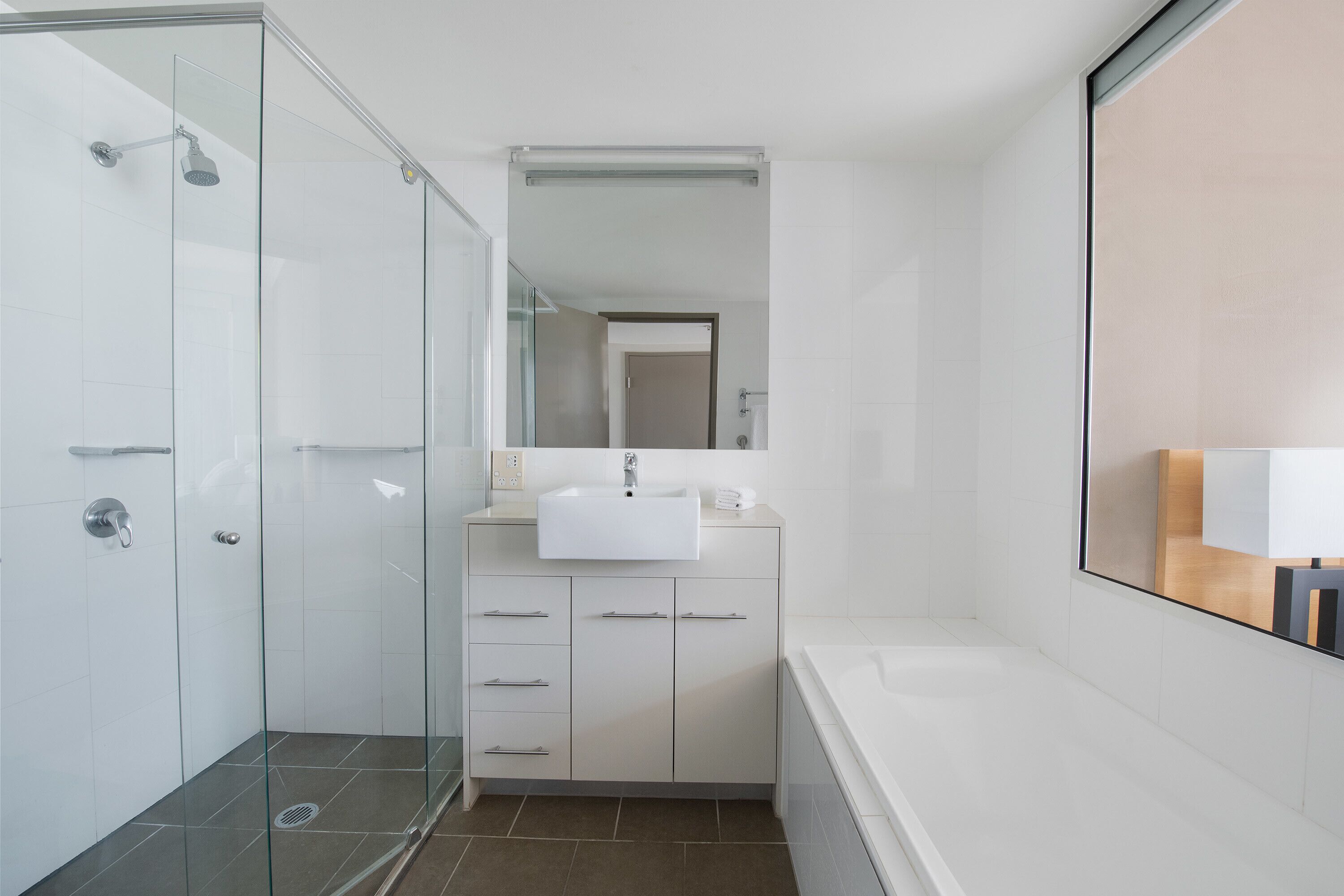 A modern bathroom with a glass shower enclosure, a white sink, and a large mirror above the vanity.