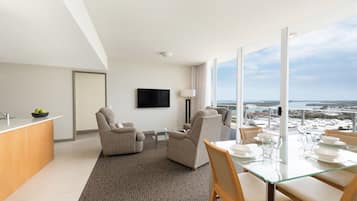 Habitación de hotel moderna con comedor, sofá, televisión y vistas a la ciudad y al mar.