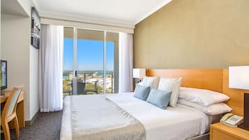 Habitación de hotel con una cama grande, un escritorio, una silla, un teléfono y vistas a la ciudad a través de una puerta corredera.