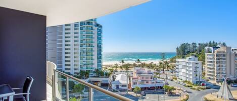 A balcony with a view of the beach and ocean, modern buildings, and a clear sky.