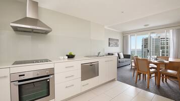A modern kitchen with built-in appliances, a dining area with a wooden table and chairs, and a large window offering a city view.