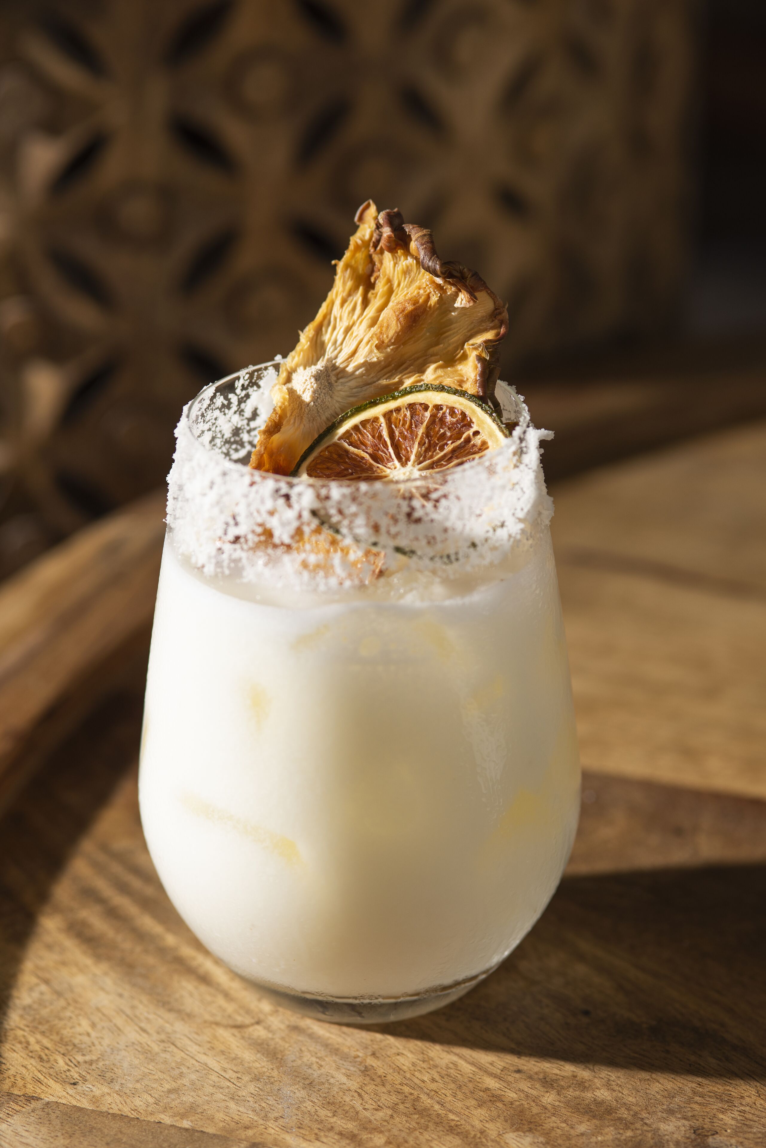 A cocktail with a salted rim and a slice of dried fruit on top, served in a glass.