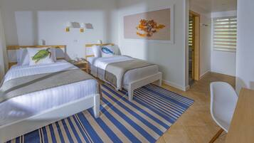 Une chambre d’hôtel avec deux lits, un bureau, une chaise, un tapis à rayures et un tableau au mur.