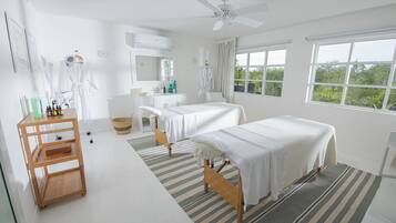 Two single beds with white linens, a desk, and a large window offering a view of the outdoors.