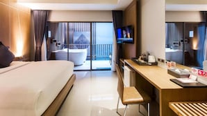 A modern hotel room with a large bed, a desk with a chair, a flat-screen TV, and a balcony with a view.