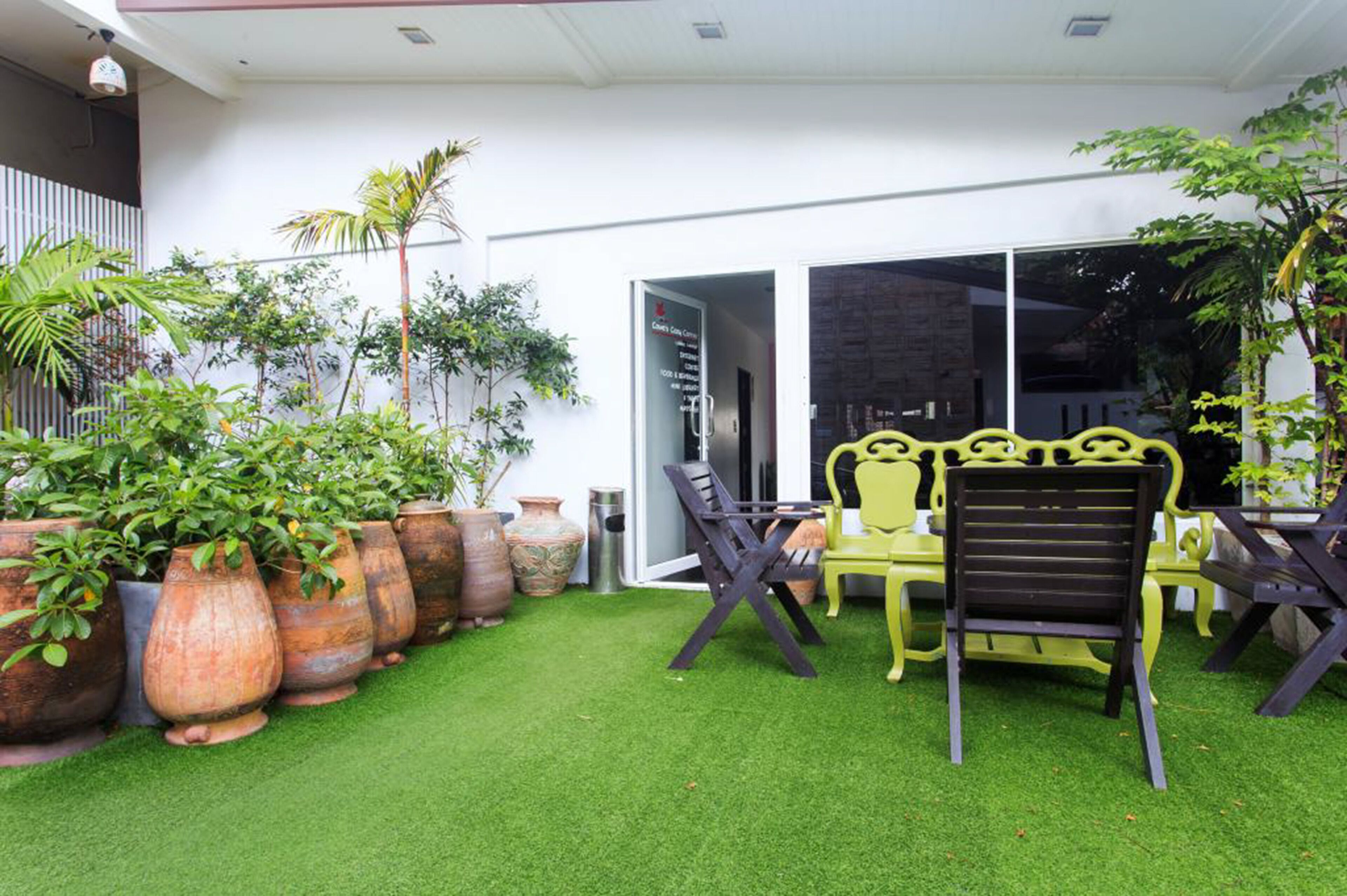 A patio with artificial grass, outdoor furniture, and large potted plants.