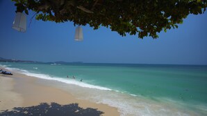 A beach with clear turquoise water, a sandy shore, and a few people swimming.