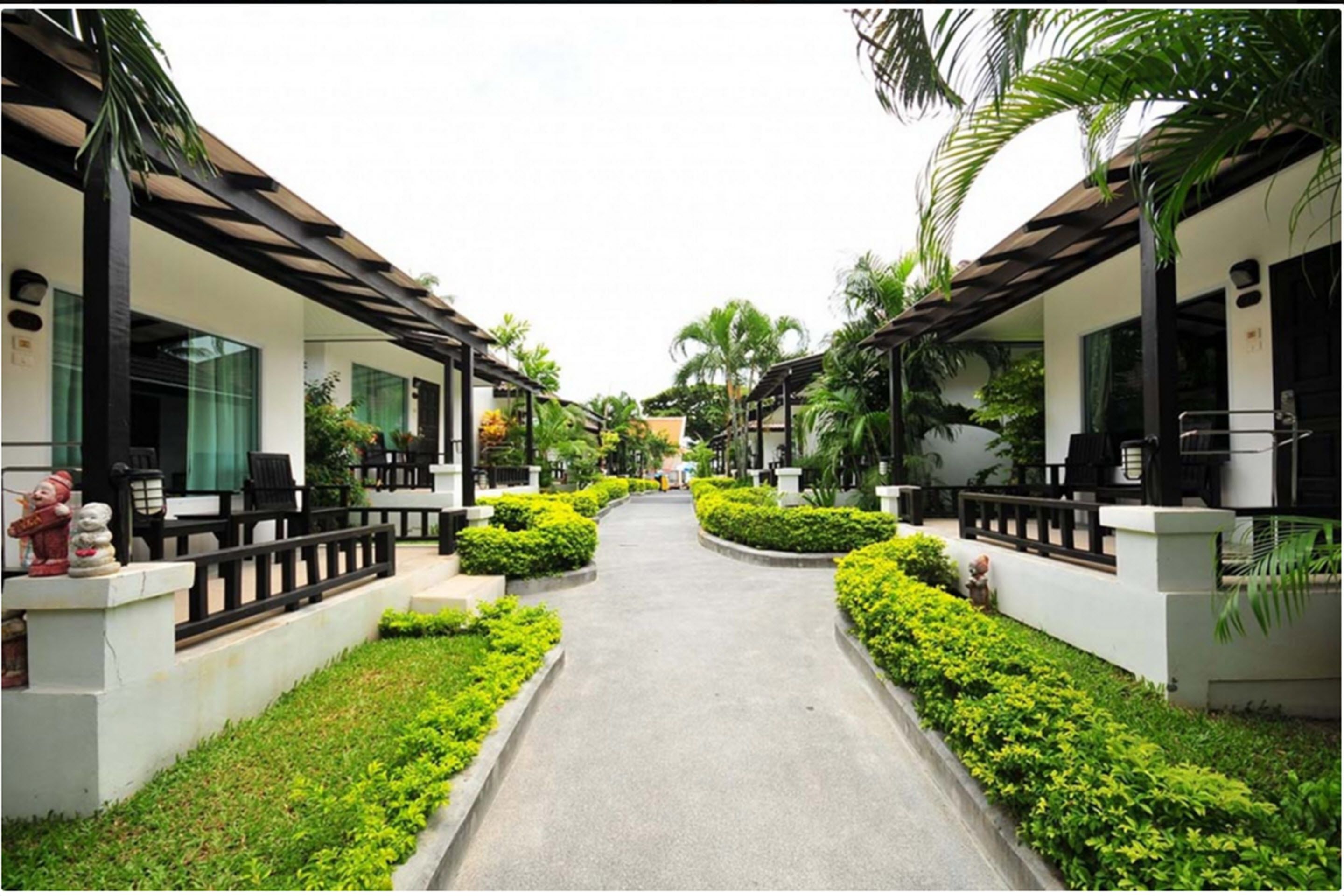 A pathway flanked by two-story buildings with balconies, surrounded by well-maintained greenery and palm trees.