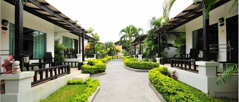 A pathway flanked by two-story buildings with balconies, surrounded by well-maintained greenery and palm trees.