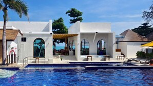 A modern resort with a pool, outdoor seating, and a view of the ocean.