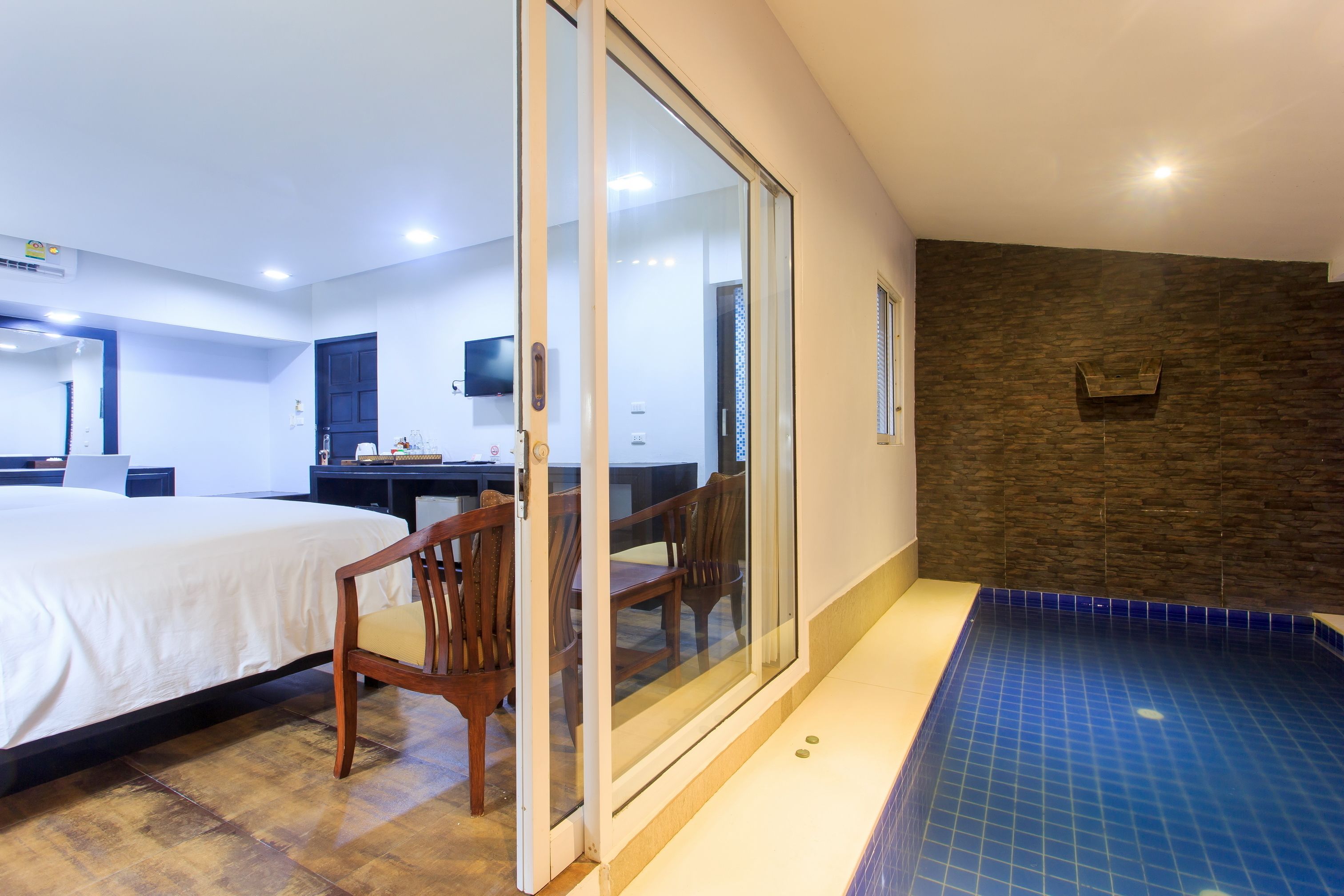 A hotel room with a bed, a desk, a chair, a sliding glass door, and a small pool area.