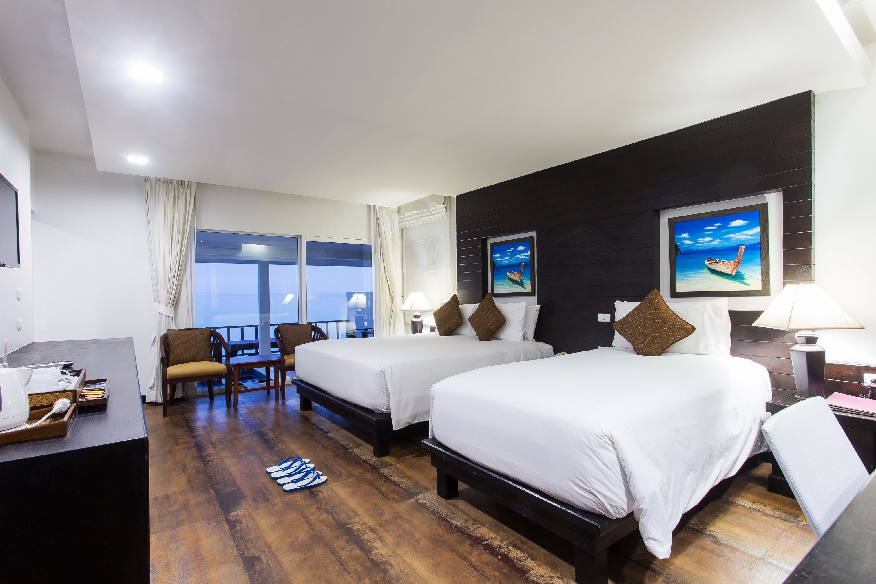 A hotel room with two beds, a desk, a chair, a window with curtains, and artwork on the wall.