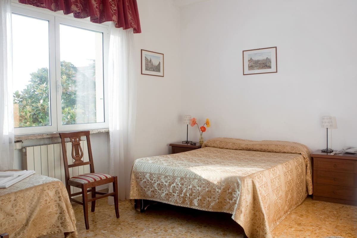 A bedroom with a bed, a chair, a nightstand, and a window with curtains.