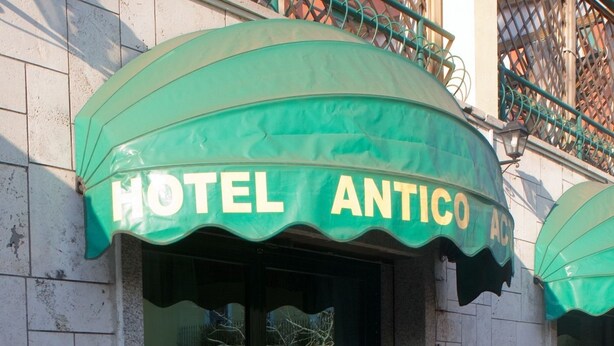 L’entrée de l’hôtel Antico se distingue par son auvent vert, ses portes vitrées et les deux plantes en pot qui la flanquent.