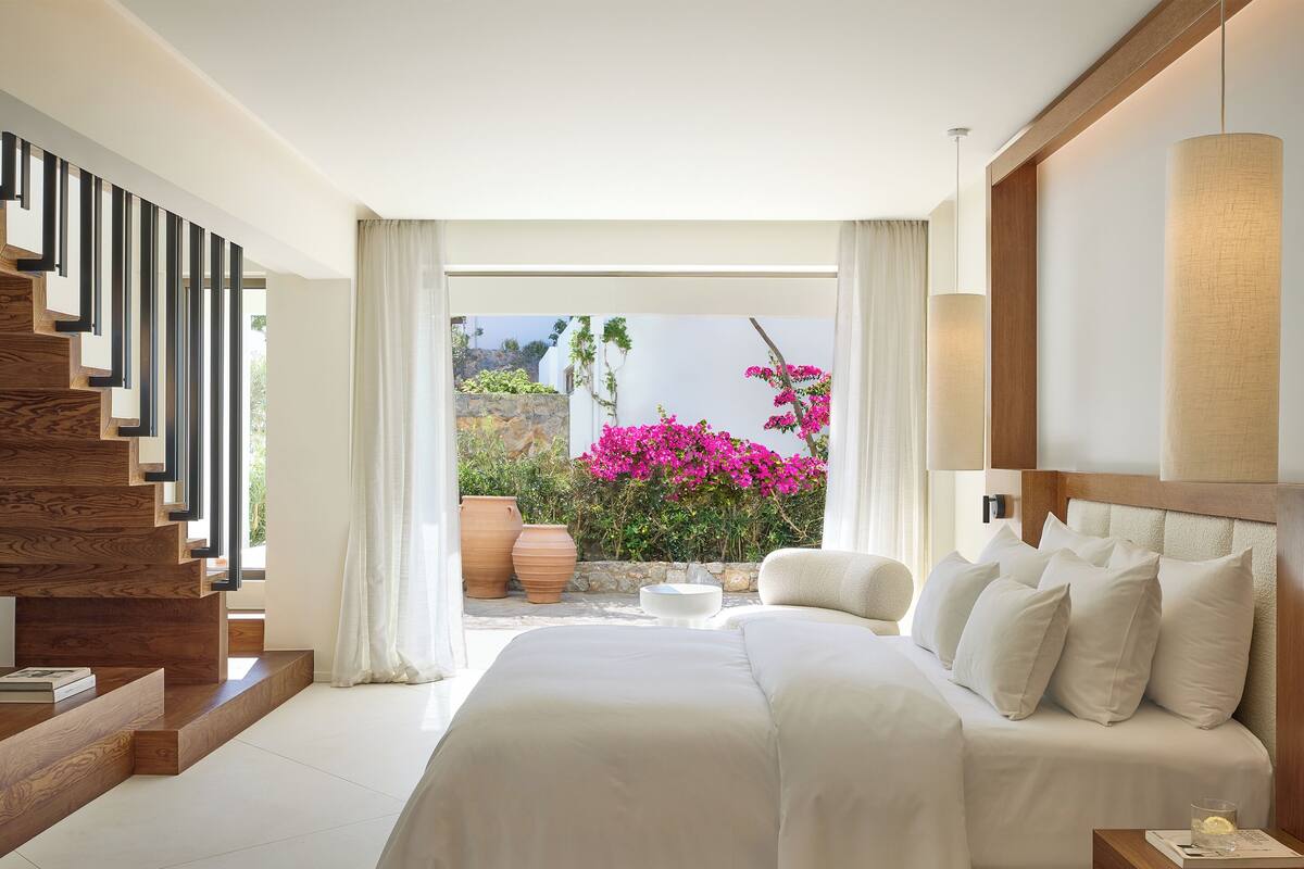 Ein modernes Schlafzimmer mit einem großen Bett, einer Holztreppe und Blick auf einen Garten mit rosa Blumen.