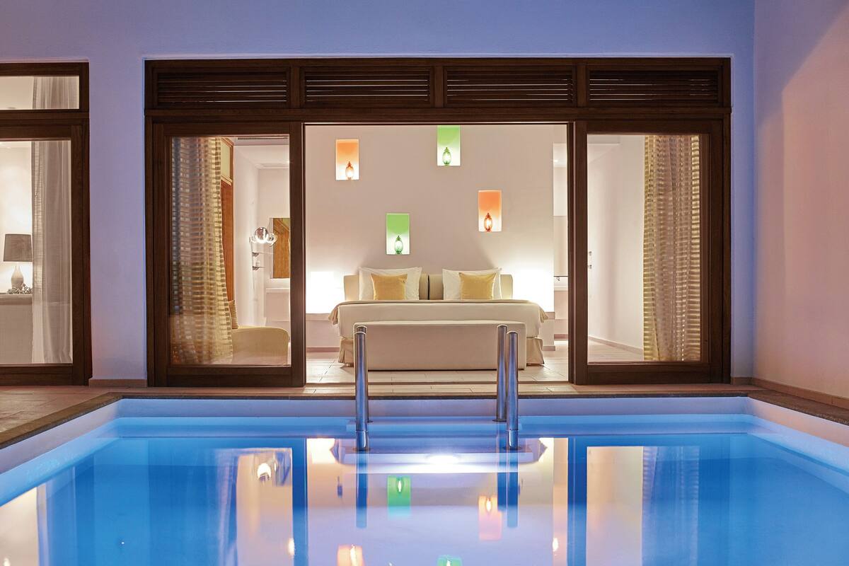 Ein Schwimmbad mit Metallleiter, ein Bett mit weißer Bettwäsche sowie ein Badezimmer mit Spiegel und Handtuchhalter.