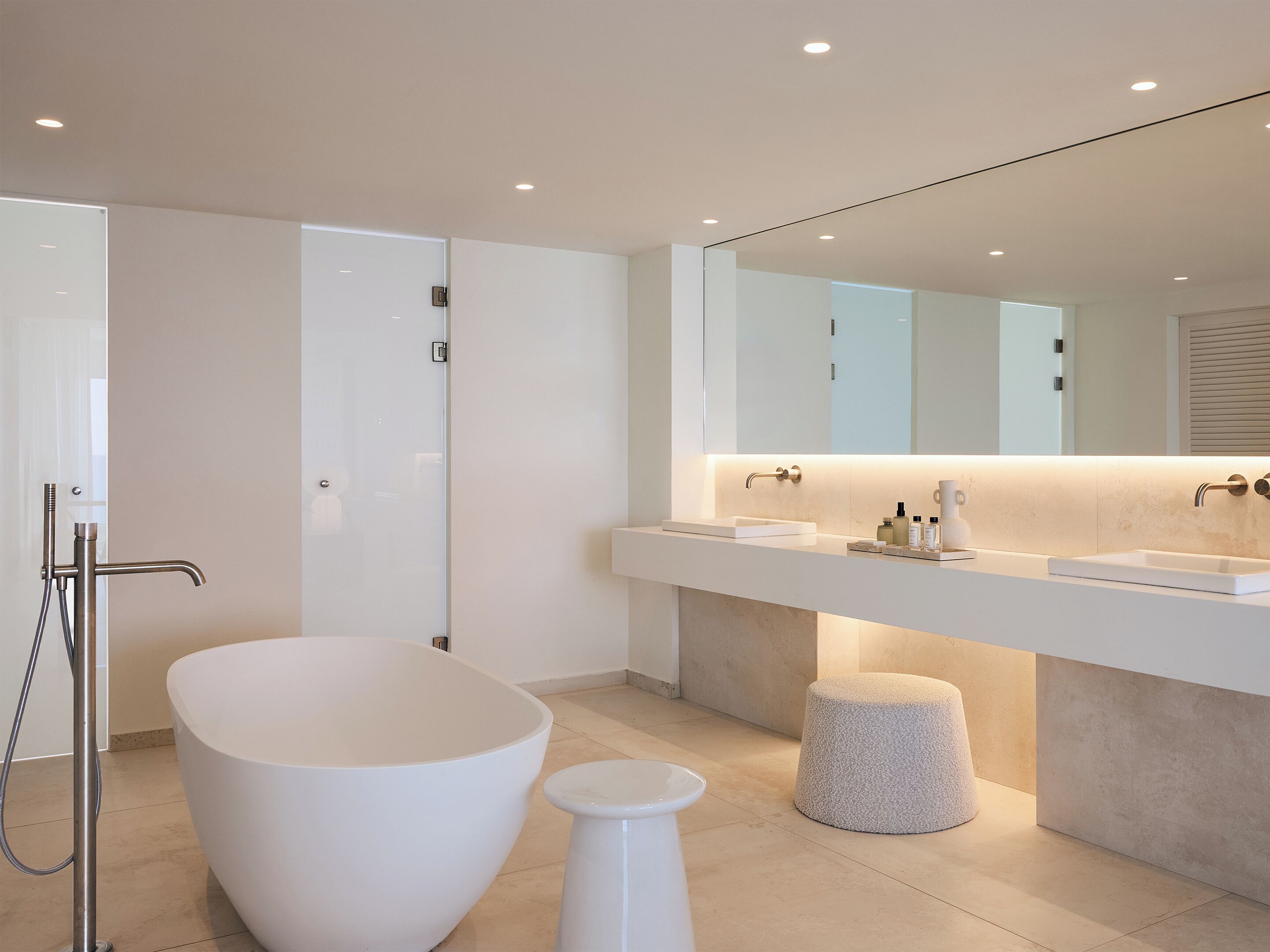 A modern bathroom with a freestanding bathtub, a large mirror, and a countertop with toiletries.