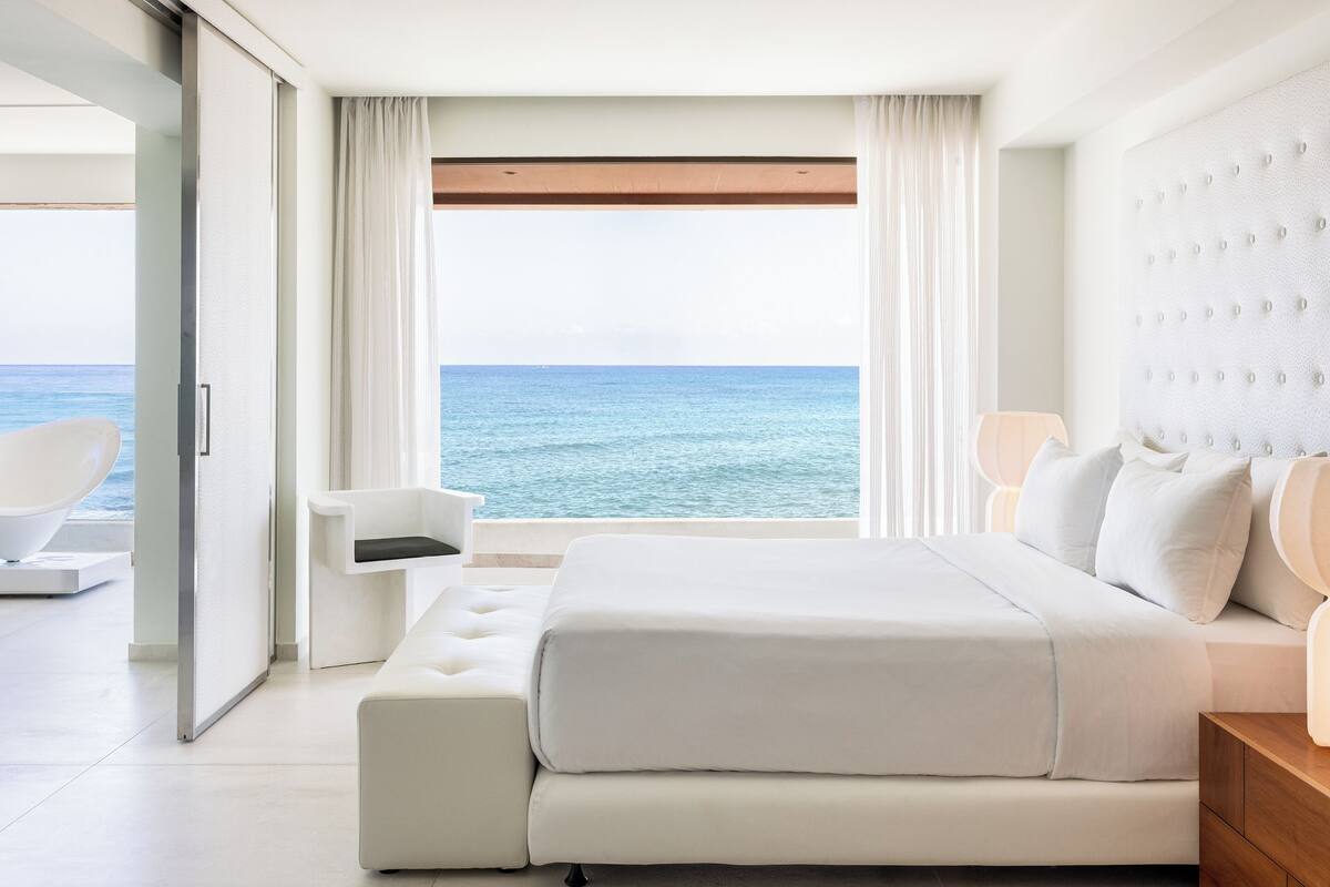 Ein modernes Schlafzimmer mit einem großen Bett, einem Sessel und Blick auf das Meer.