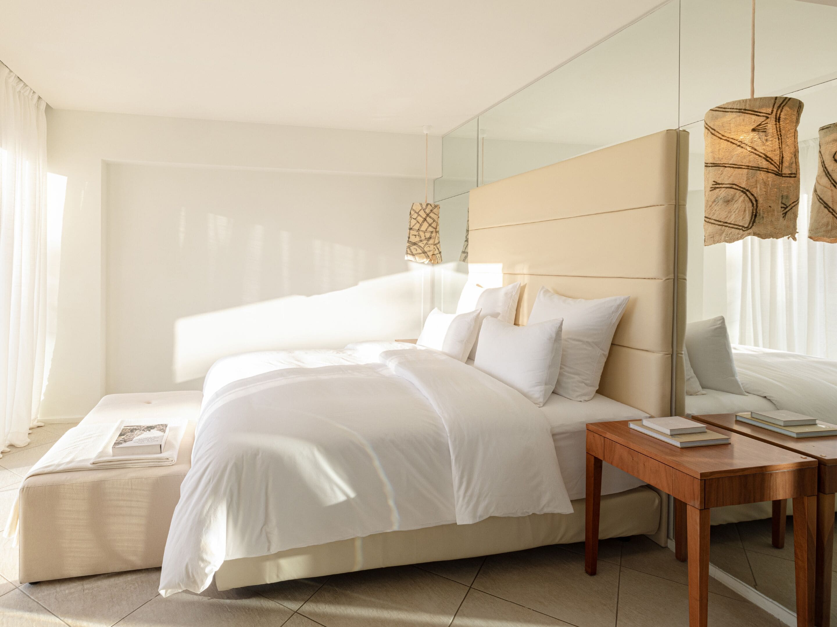 Une chambre d’hôtel moderne avec un grand lit, une table de chevet avec des livres et un grand miroir.