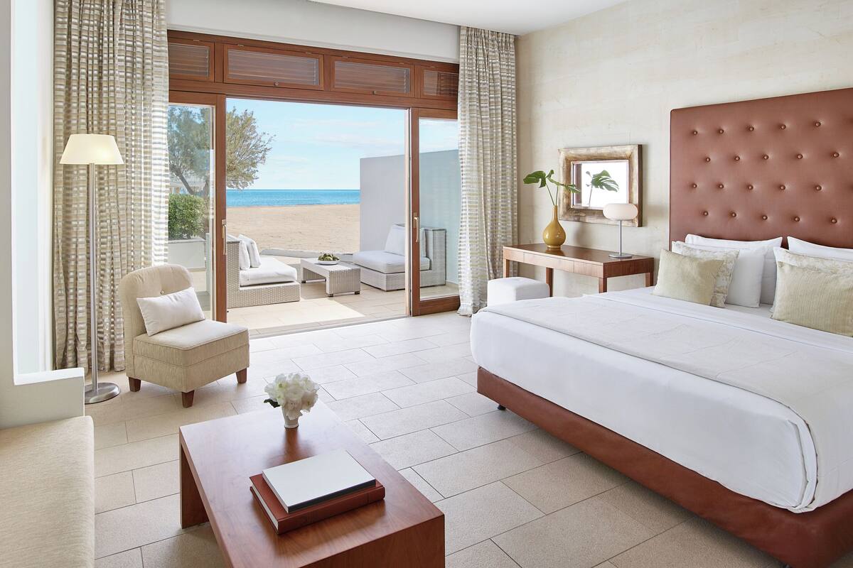 Ein Hotelzimmer mit einem großen Bett, einem Schreibtisch, einem Sessel und Blick auf den Strand.