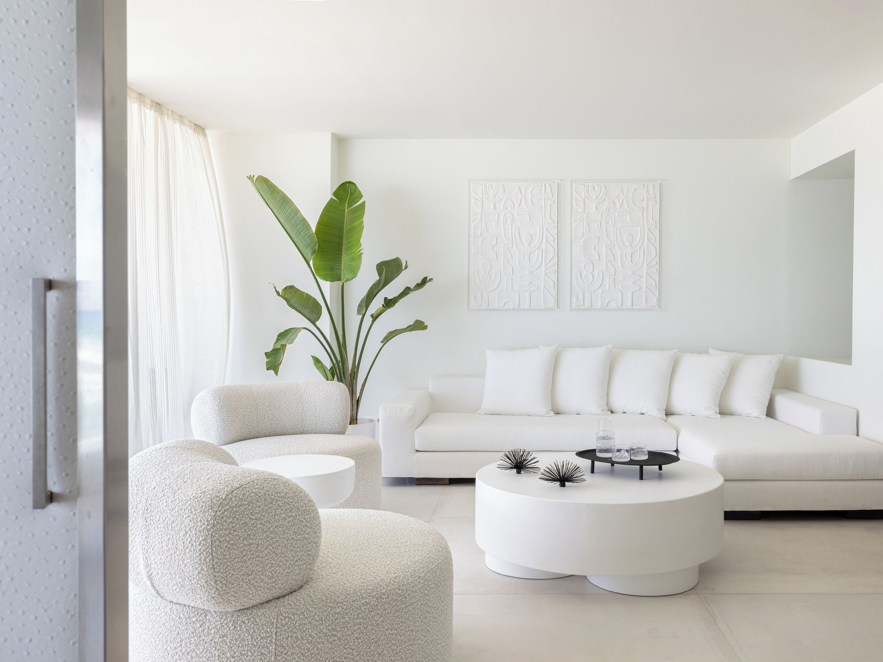 Ett modernt vardagsrum med en vit soffa, ett runt soffbord och en stor växt.