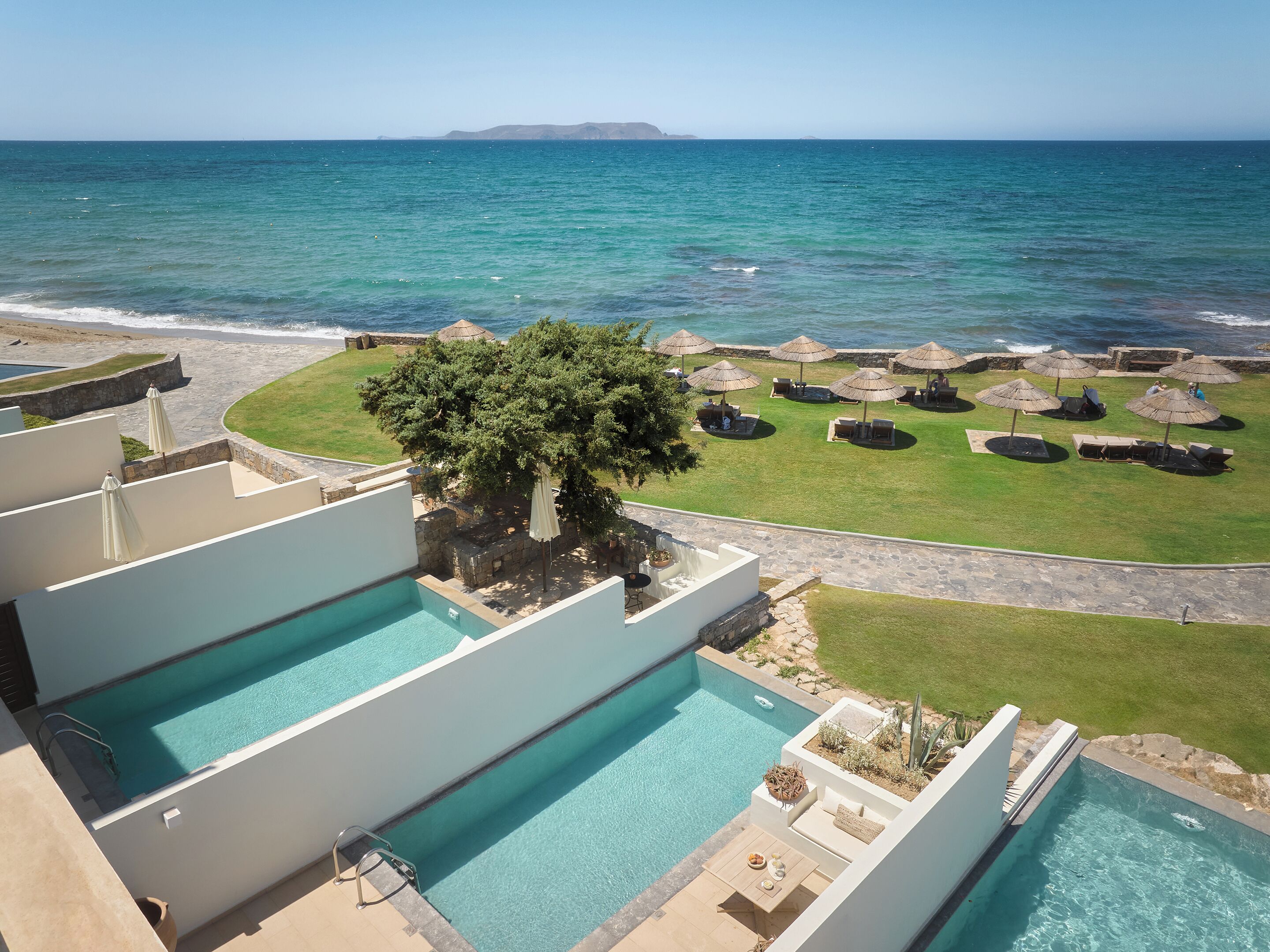 Una piscina en la azotea con vista al océano, un área de césped con sombrillas y un camino de piedra.