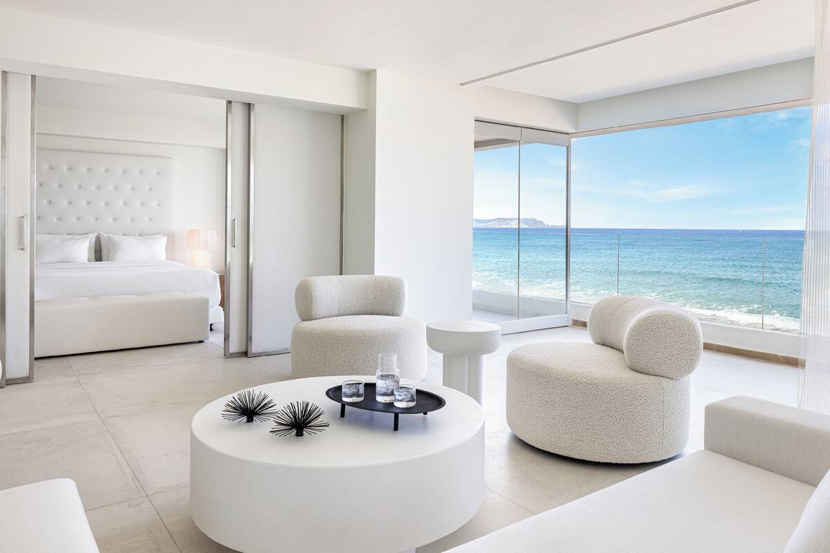 Ein modernes Hotelzimmer mit einem Bett, zwei Sesseln, einem Couchtisch und Meerblick.