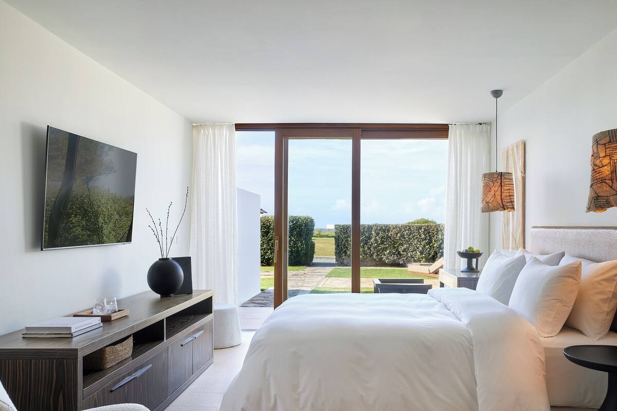 Ein modernes Schlafzimmer mit einem großen Bett, einem Fernseher, einem Konsolentisch und Blick ins Freie.