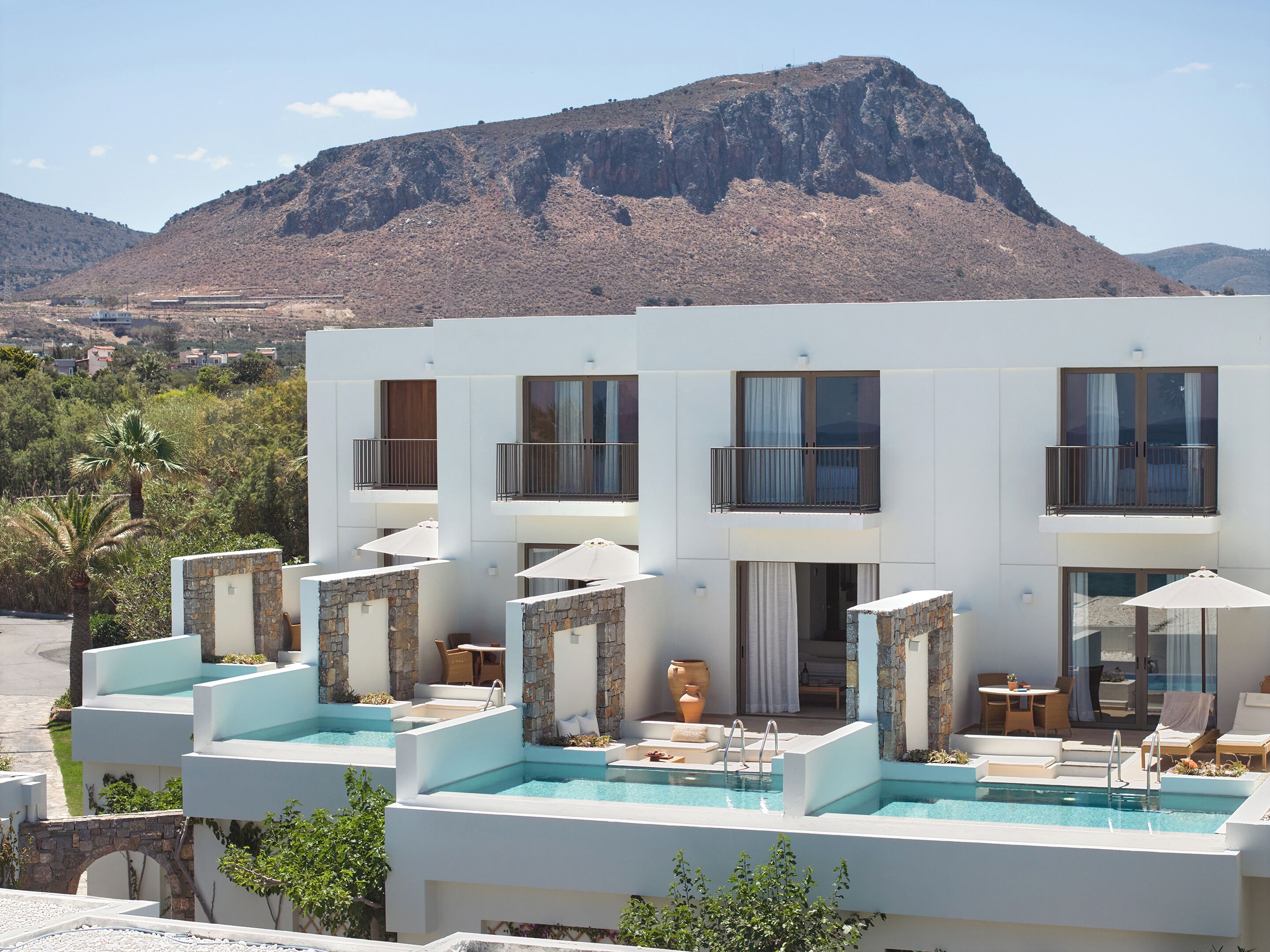 A modern hotel with a pool area, stone walls, and balconies overlooking a mountainous landscape.