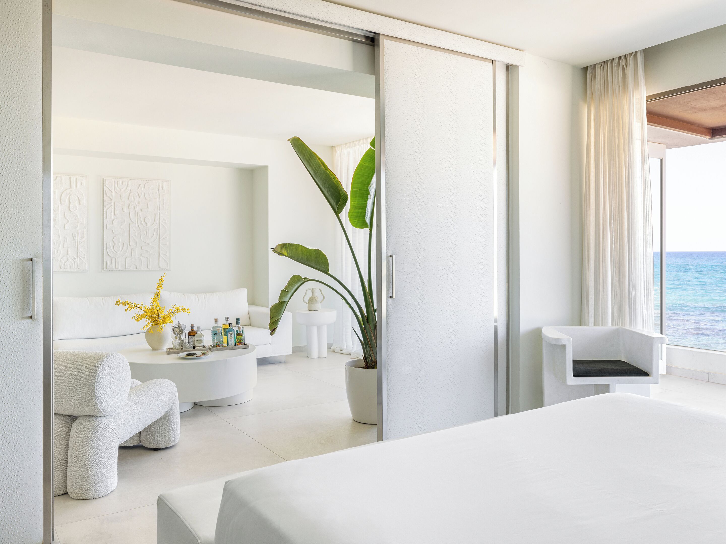 Ein modernes Hotelzimmer mit einem Bett, einer Sitzecke mit Couchtisch, einer Pflanze und Meerblick.