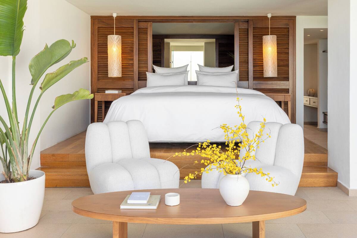 Ein modernes Hotelzimmer mit einem großen Bett, zwei Nachttischen, einem Sofa, einem Couchtisch und einer Zimmerpflanze.