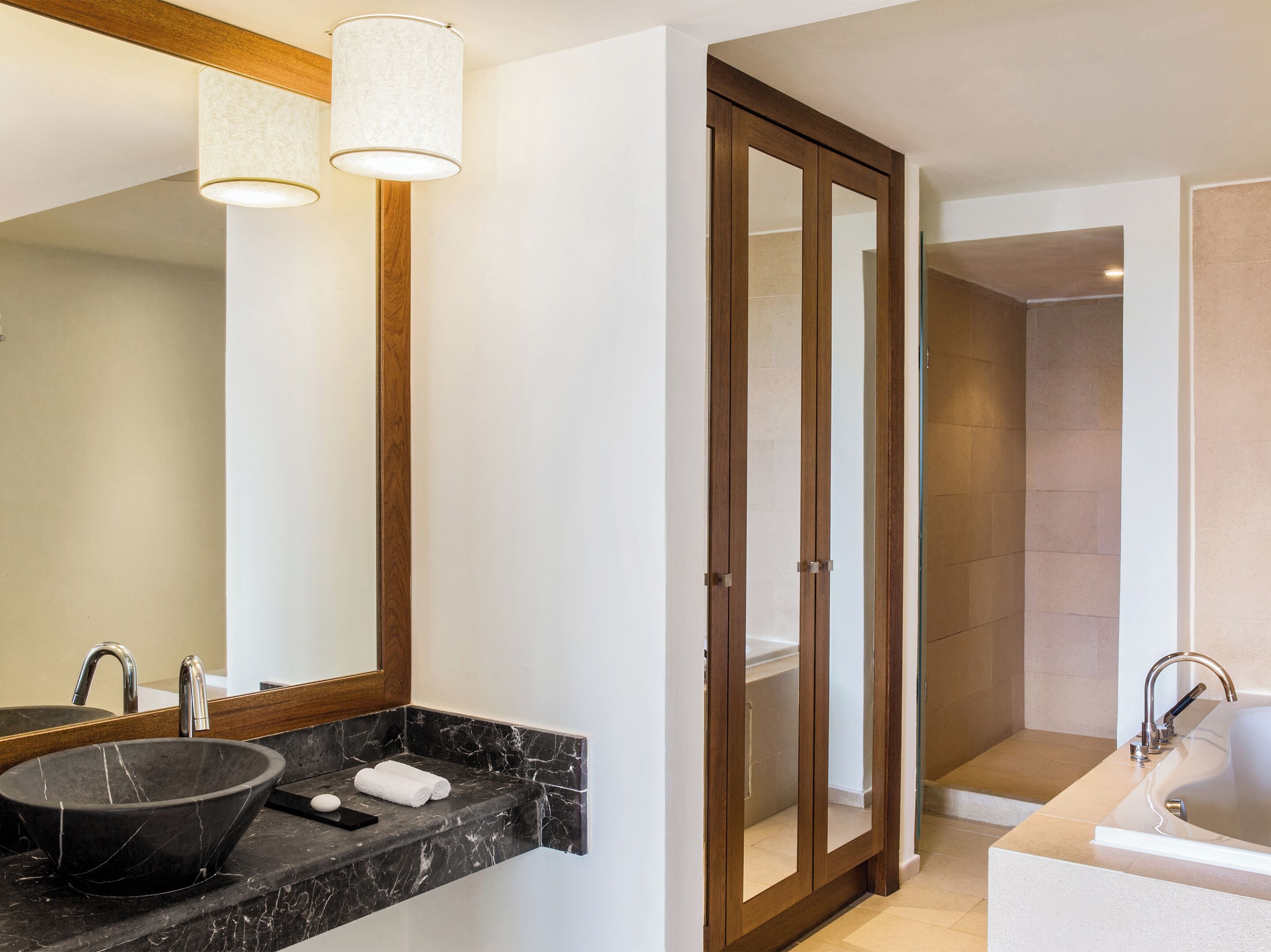 A modern bathroom with a marble sink, a large mirror, a wooden door, and a separate shower area.