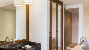 A modern bathroom with a marble sink, a large mirror, a wooden door, and a separate shower area.