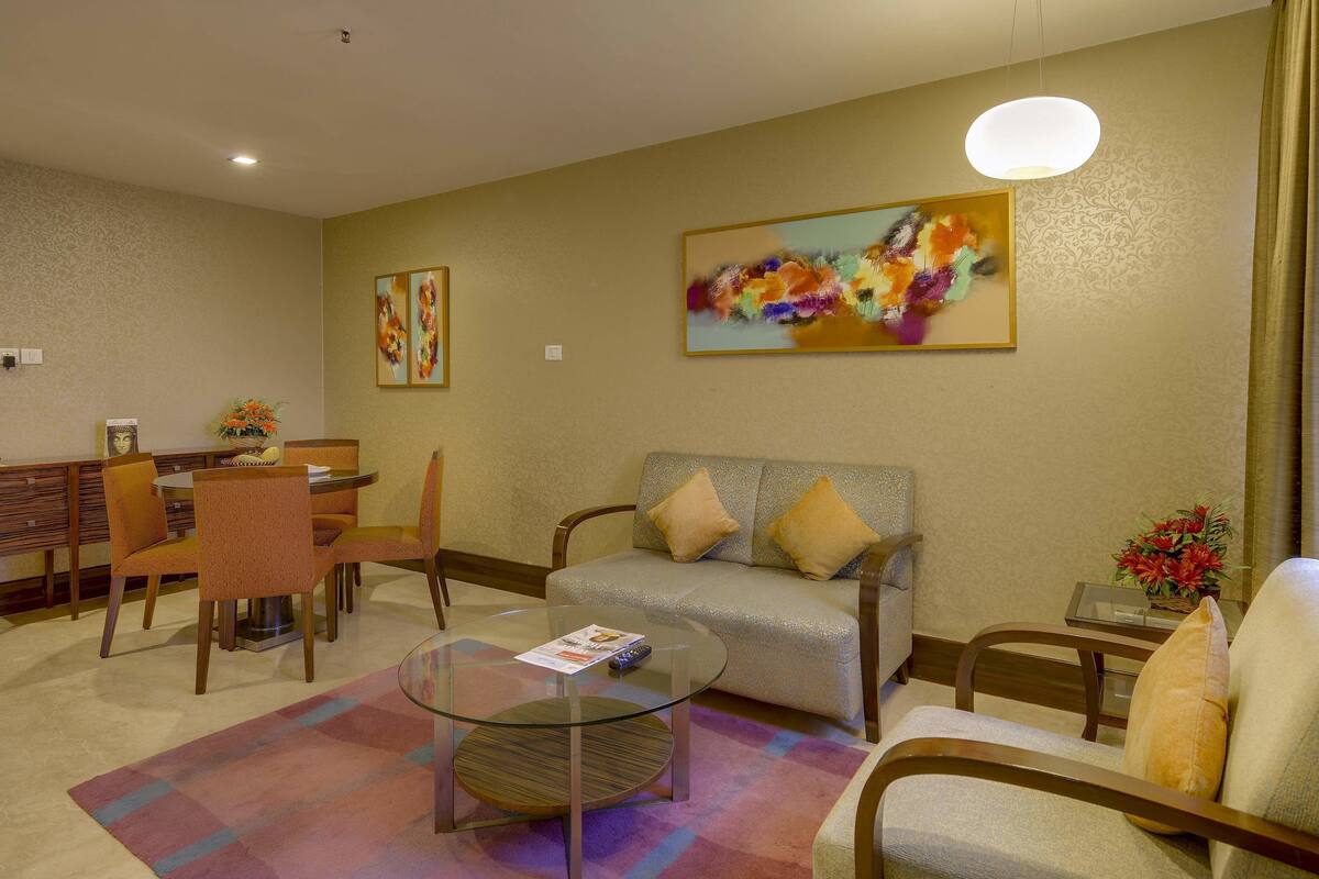 Une chambre d’hôtel comprenant un coin repas, un canapé, une table basse en verre et un tableau au mur.