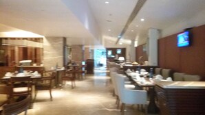 Un couloir d’hôtel avec des tables et des chaises, un téléviseur fixé au mur et, au fond, un espace d’accueil.
