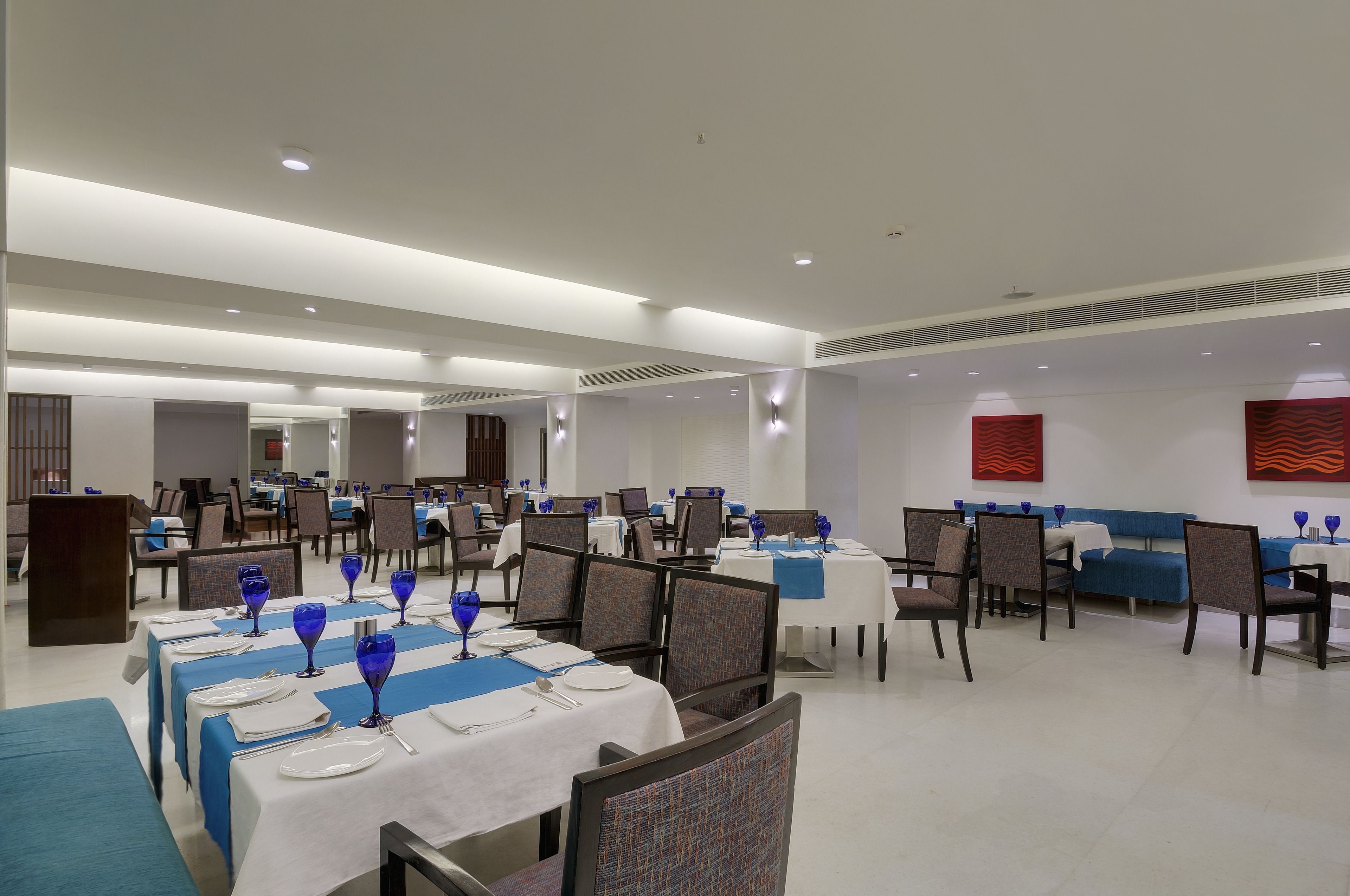 A spacious dining area with multiple tables set for service, featuring blue tablecloths and matching glassware.