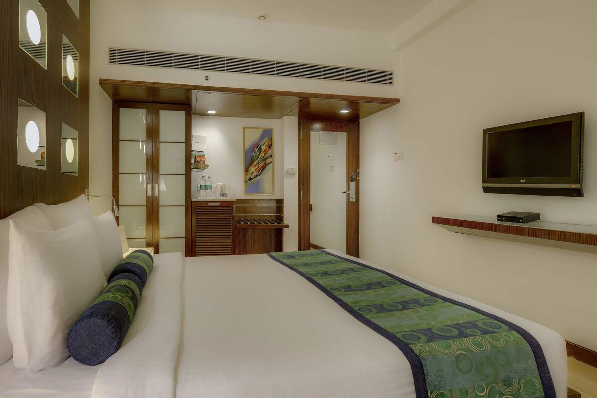 Une chambre d’hôtel avec un lit, un téléviseur fixé au mur, une armoire en bois et un miroir avec éclairage intégré.